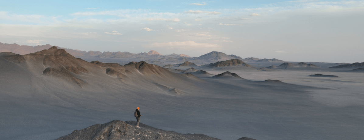Imagem de um homem no topo de um morro e ao fundo montanhas em um ambiente deserto