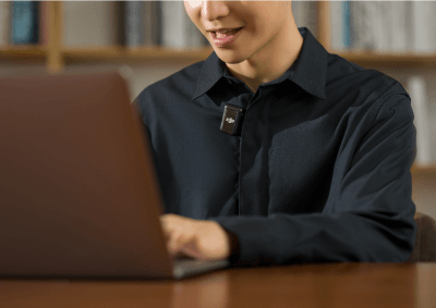 Foto de um homem mexendo em um laptop, enquanto que no colarinho de sua camisa social há um DJI Mic 2 realizando toda a captação de áudio